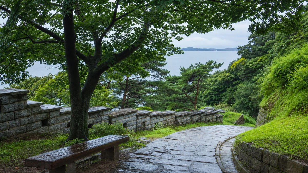 비에 젖은 성곽 산책로와 나무 사이로 보이는 바다