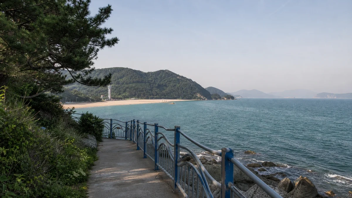 부산 송도 구름산책로의 바다 위 곡선 데크와 난간, 멀리 송도해수욕장과 해안 도시가 보이는 접근 장면