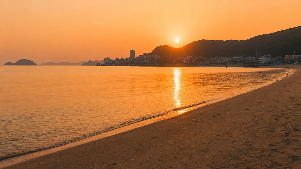 부산 송도해수욕장에 주황빛 저녁 햇살이 내려앉고 잔잔한 물결이 모래사장에 닿는 시간대 장면